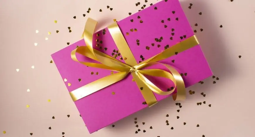 Pink Gift box with yellow ribbon and sprinkled yellow heart glitters with light pink background - Personalized Gifts